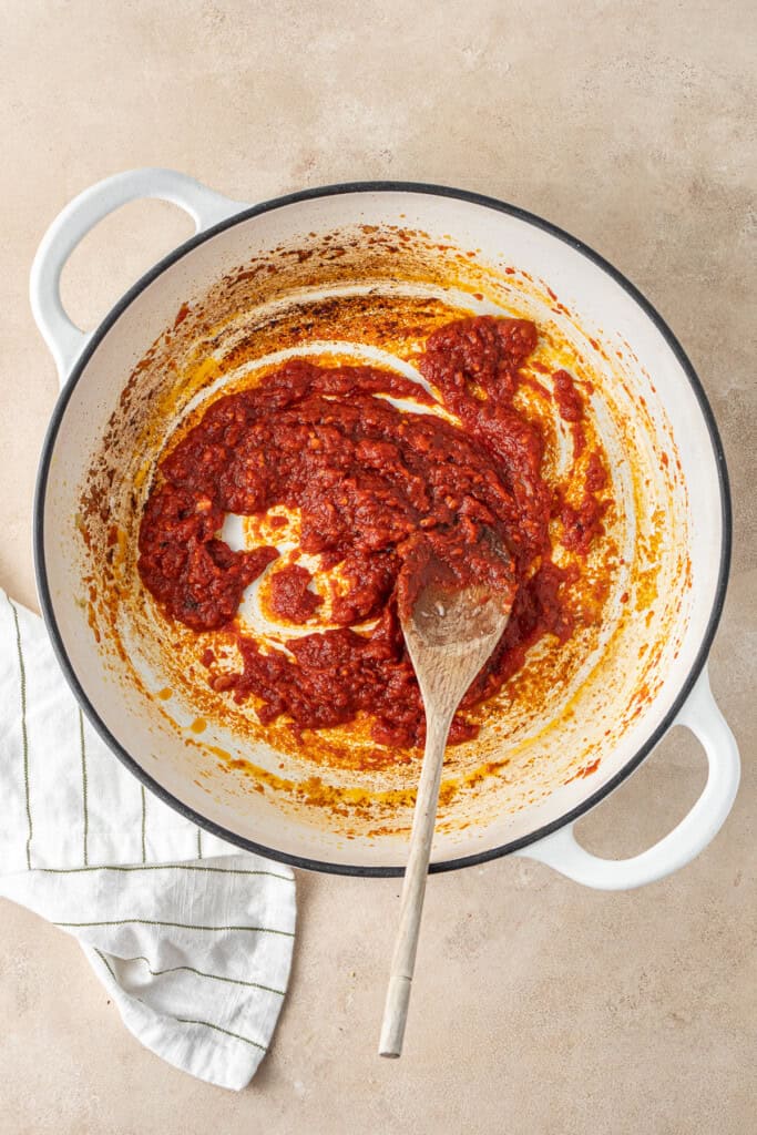 Mixing in the tomato paste to the onions in the pot.