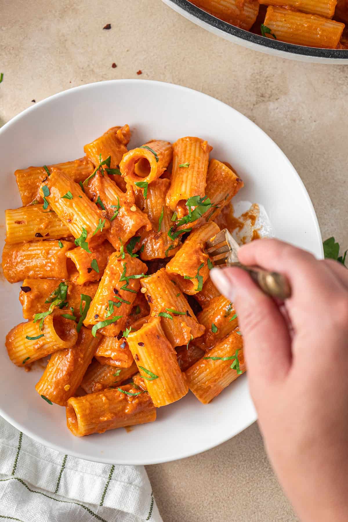 A hand taking a bite of the vegan vodka pasta from the bowl.