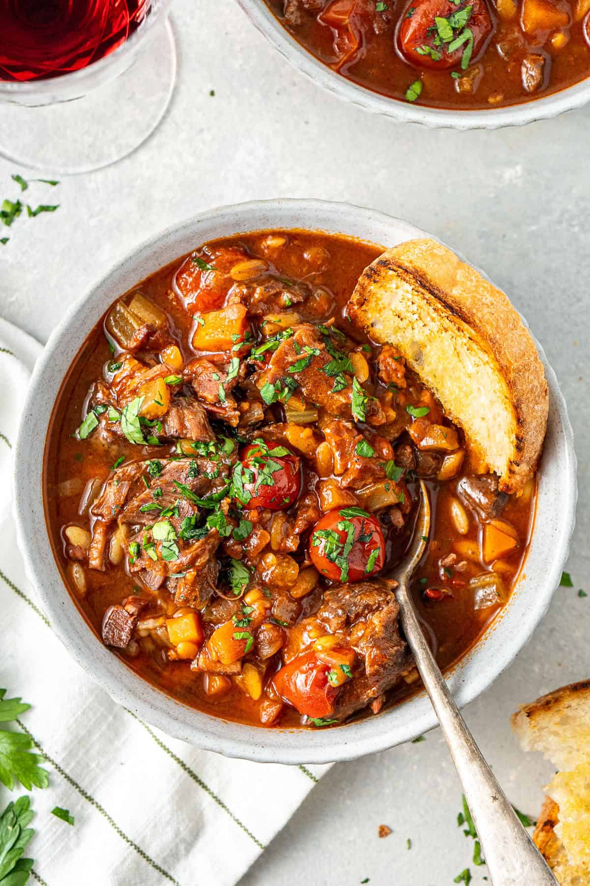 A bowl of beef minestrone soup with a slice of bread and a spoon.