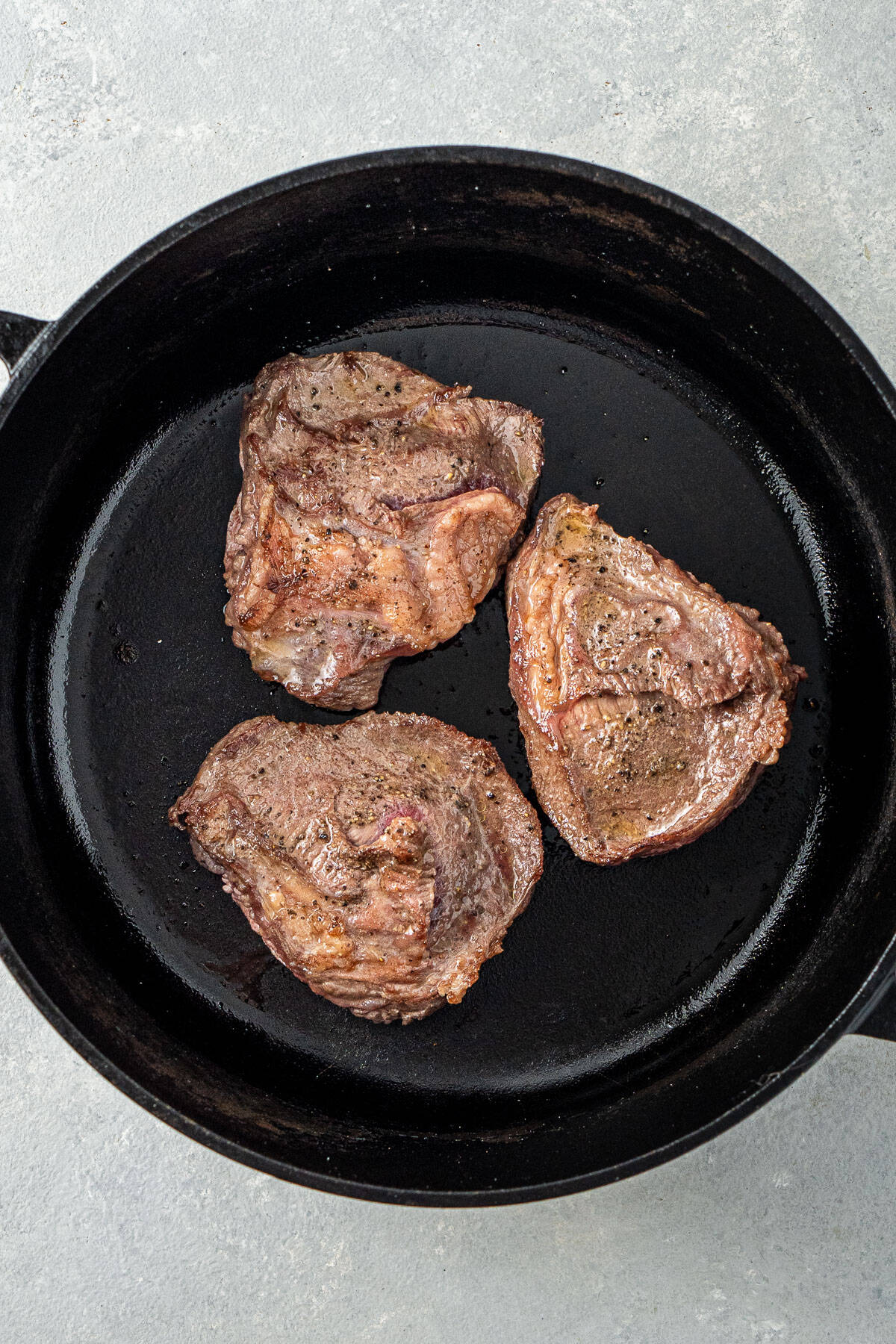 The beef cheeks being seared in a black pot.