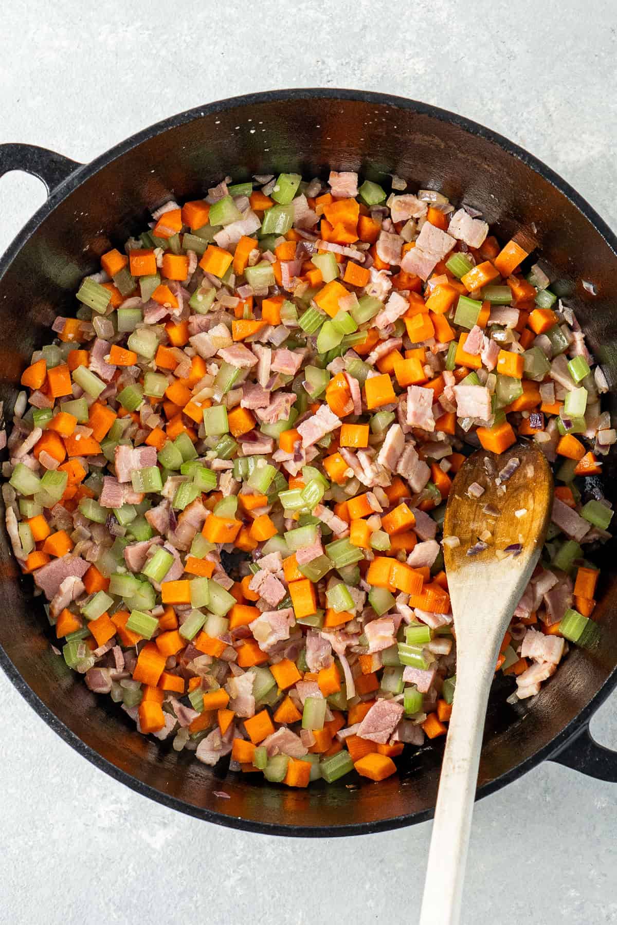 The vegetables and bacon with a wooden spoon in the pot.