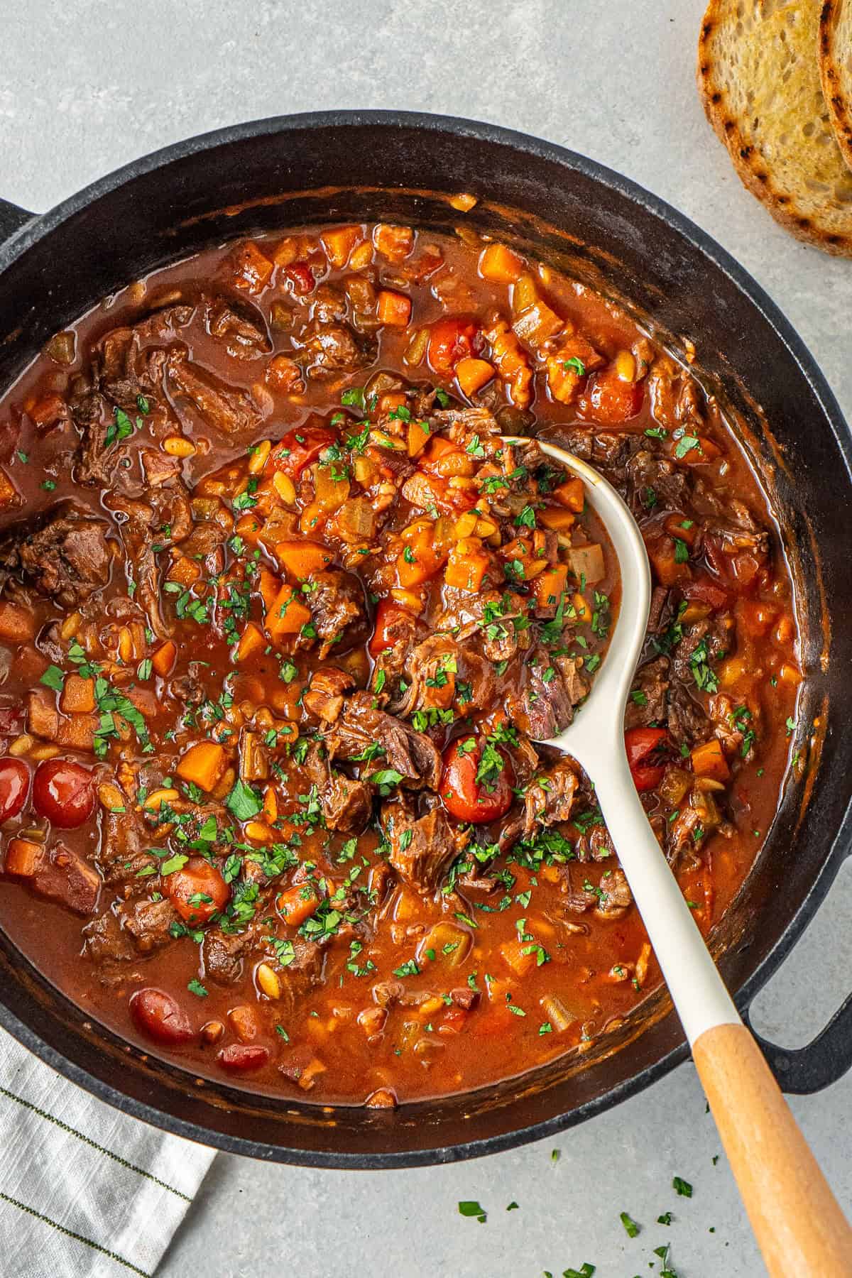 A soup ladle in the pot of soup with fresh parsley.