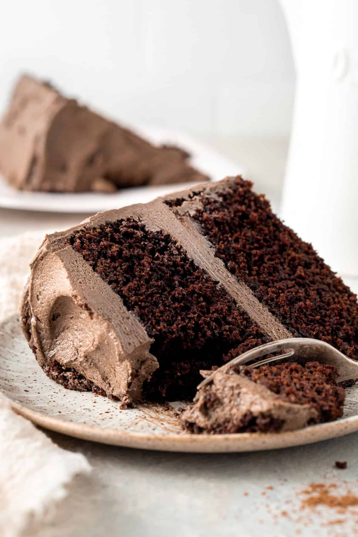 A fork taking a bite of a slice of dairy free chocolate cake on a plate.