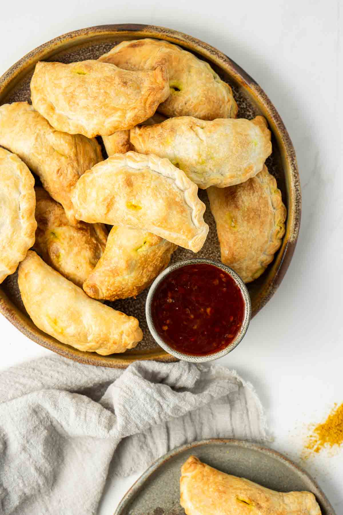 Curry puffs on a brown plate with sweet chilli sauce.