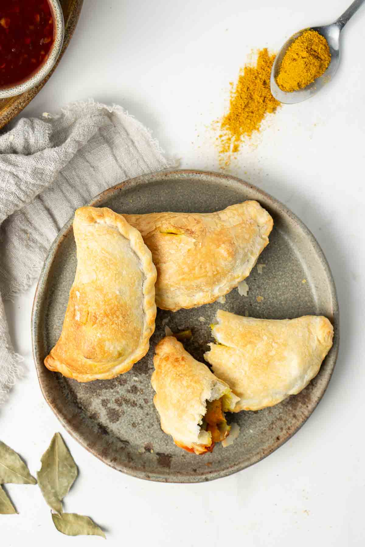 Curry puffs on a grey plate and a spoonful of curry powder.