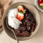 Chocolate self saucing pudding in a bowl with ice cream and strawberries.