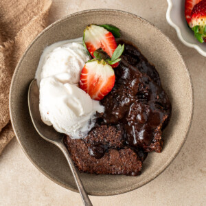 Chocolate self saucing pudding in a bowl with ice cream and strawberries.