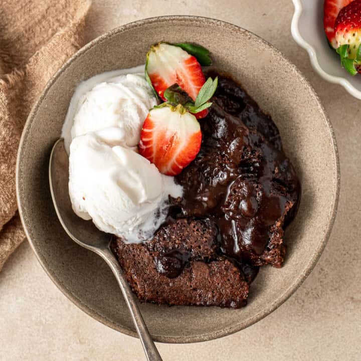 Chocolate self saucing pudding in a bowl with ice cream and strawberries.