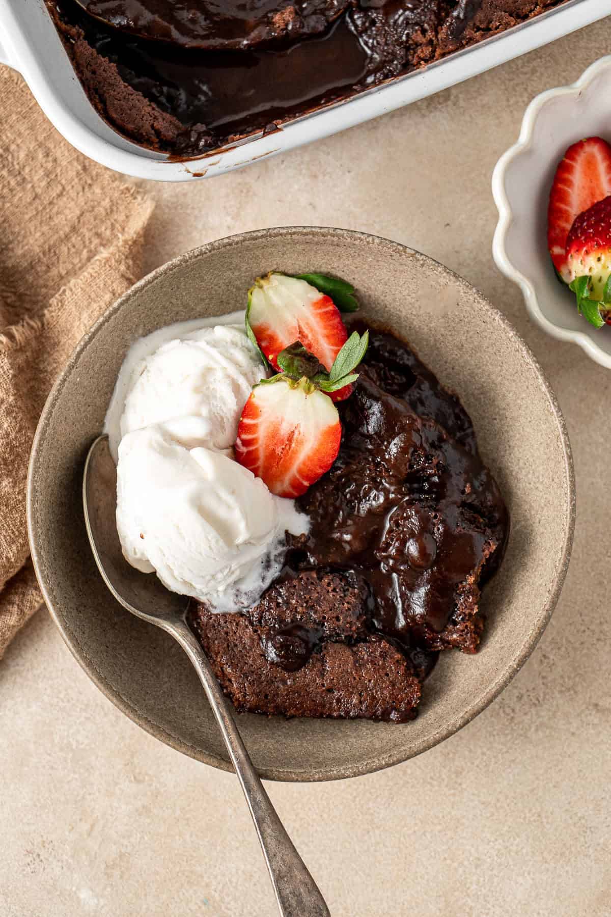 Chocolate self saucing pudding in a bowl with ice cream and strawberries.