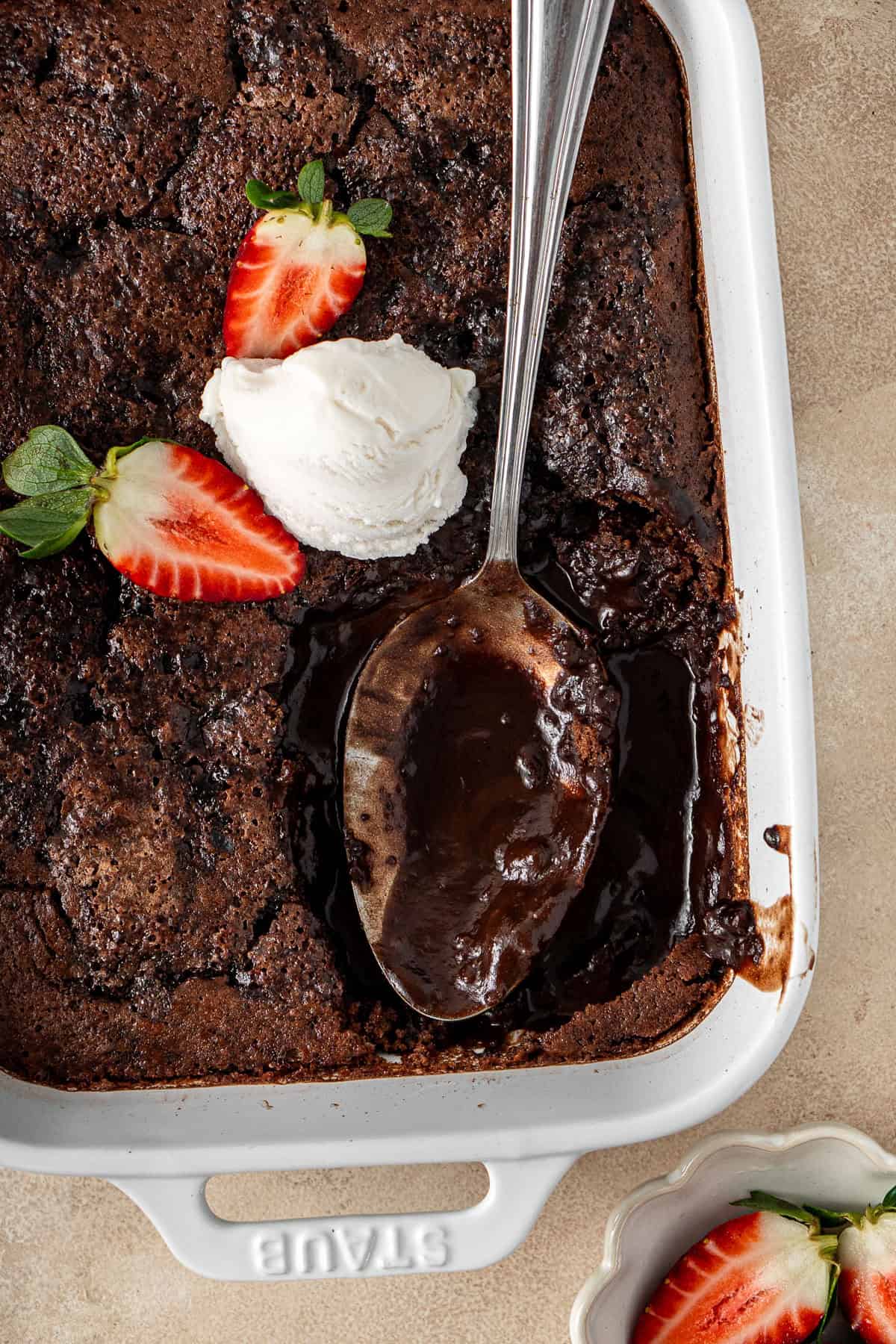 Chocolate self saucing pudding with a serving spoon, ice cream and berries.