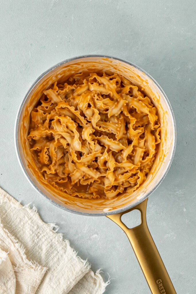 The cooked noodles tossed with the sauce in a saucepan.