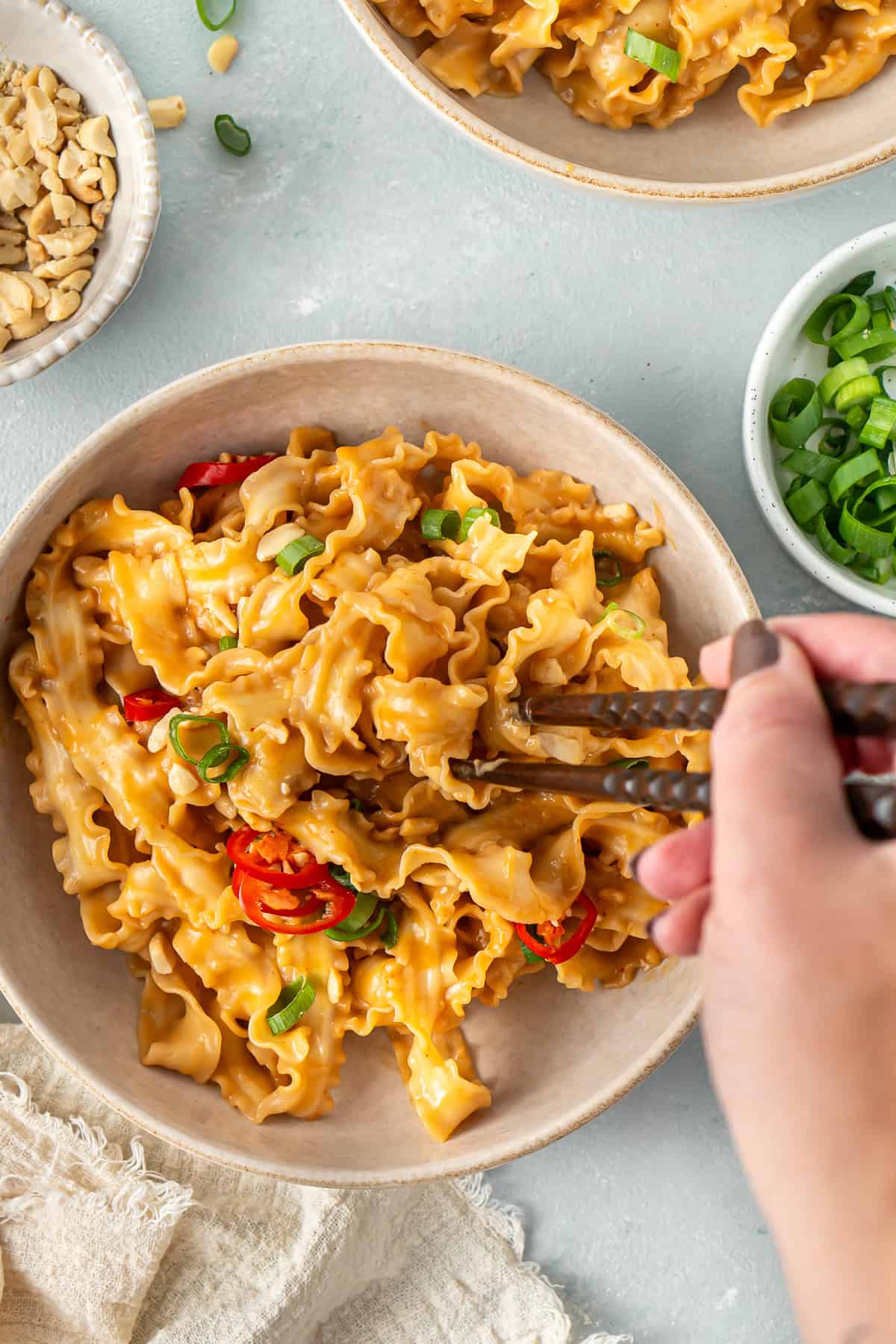 Chopsticks taking a bite of creamy peanut butter noodles.