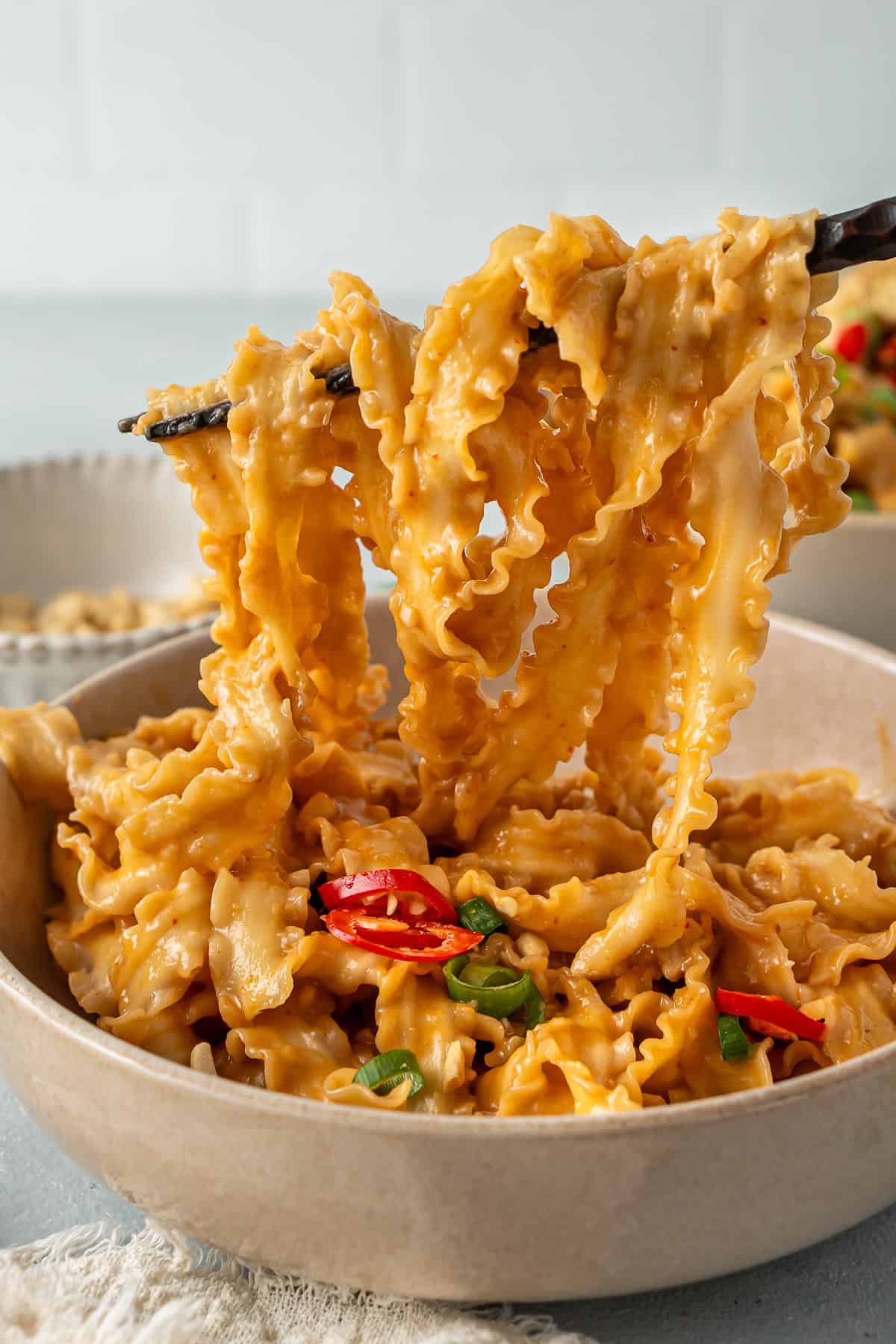 Chopsticks pulling noodles up out of the bowl showing how saucy they are.