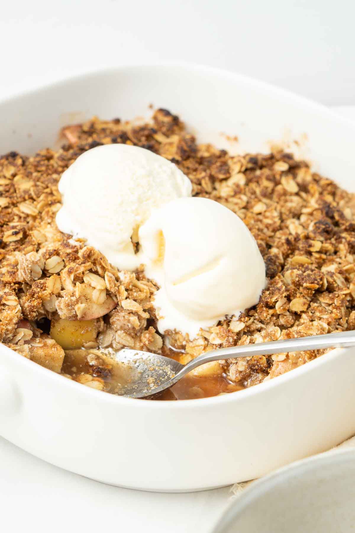 Close up of the baked vegan apple crumble with melting vanilla ice cream.