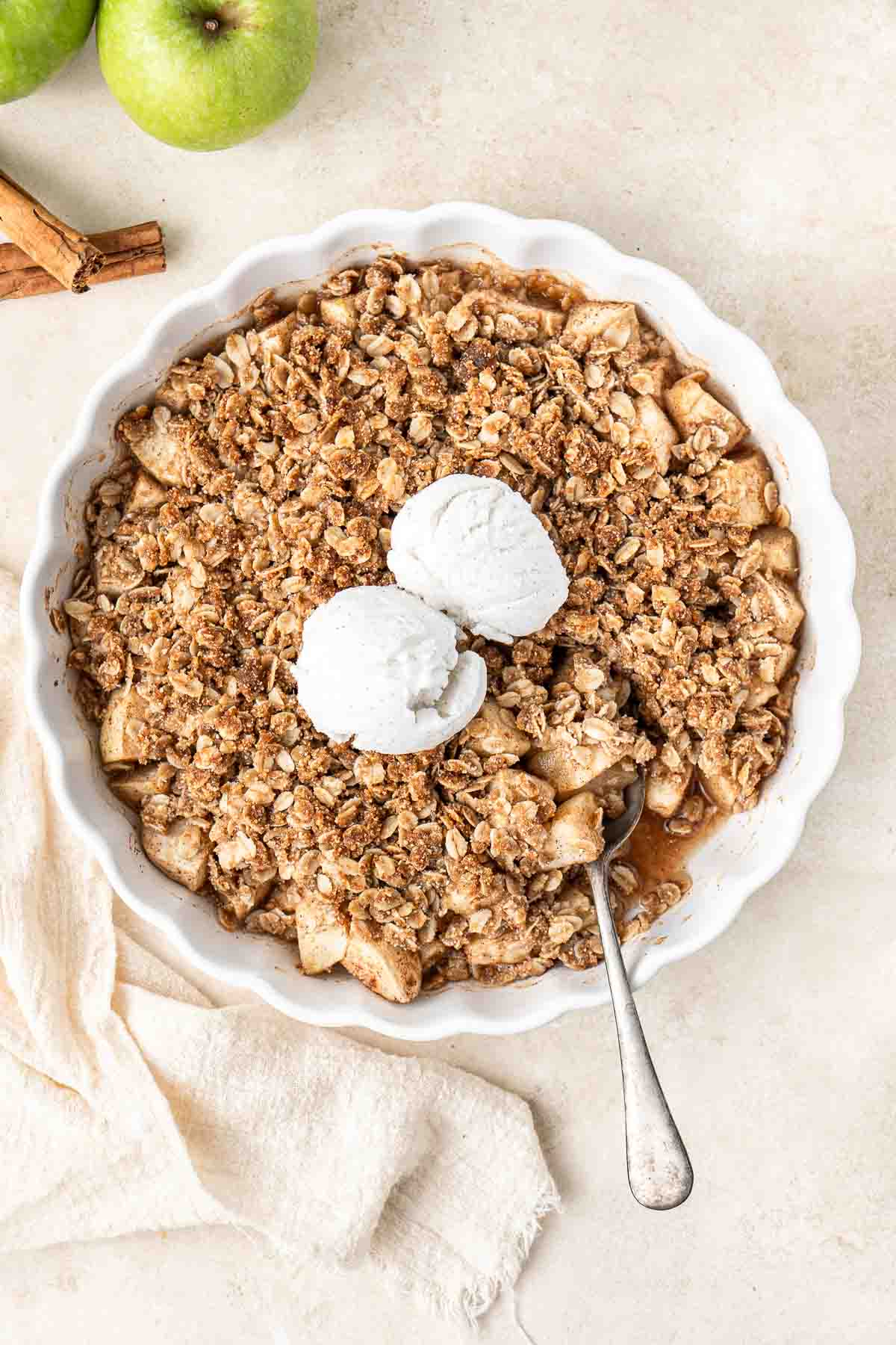 Freshly baked vegan apple crumble with vanilla ice cream and a spoon.