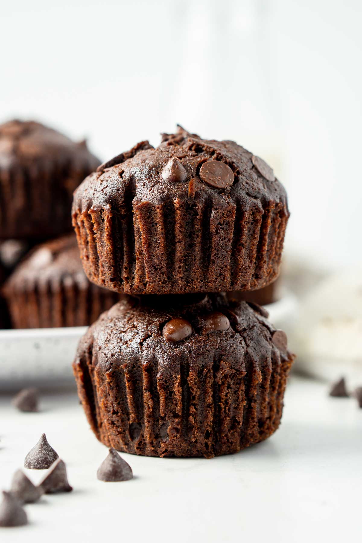 Close up of two chocolate muffins stacked together and extra chocolate chips.