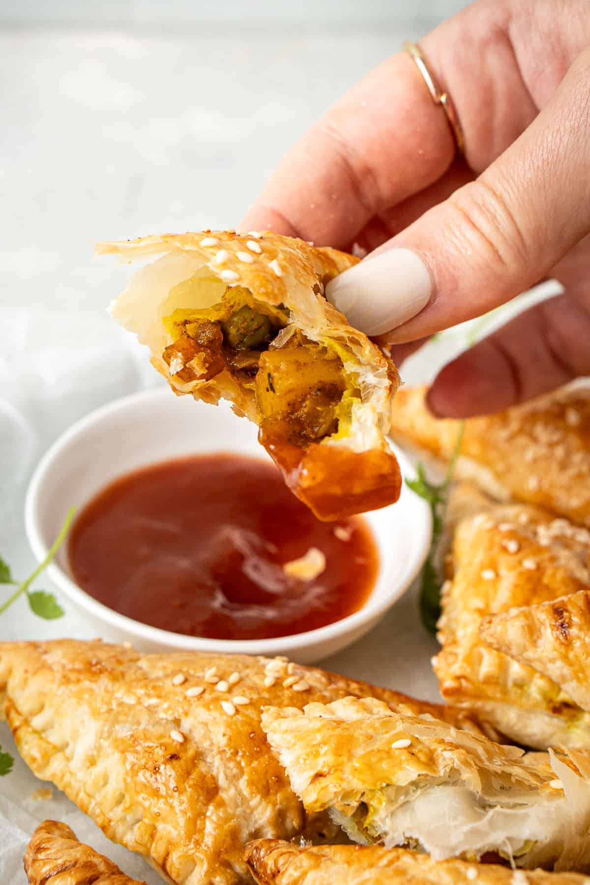 A hand holding a piece of curry puff showing the filling inside. 