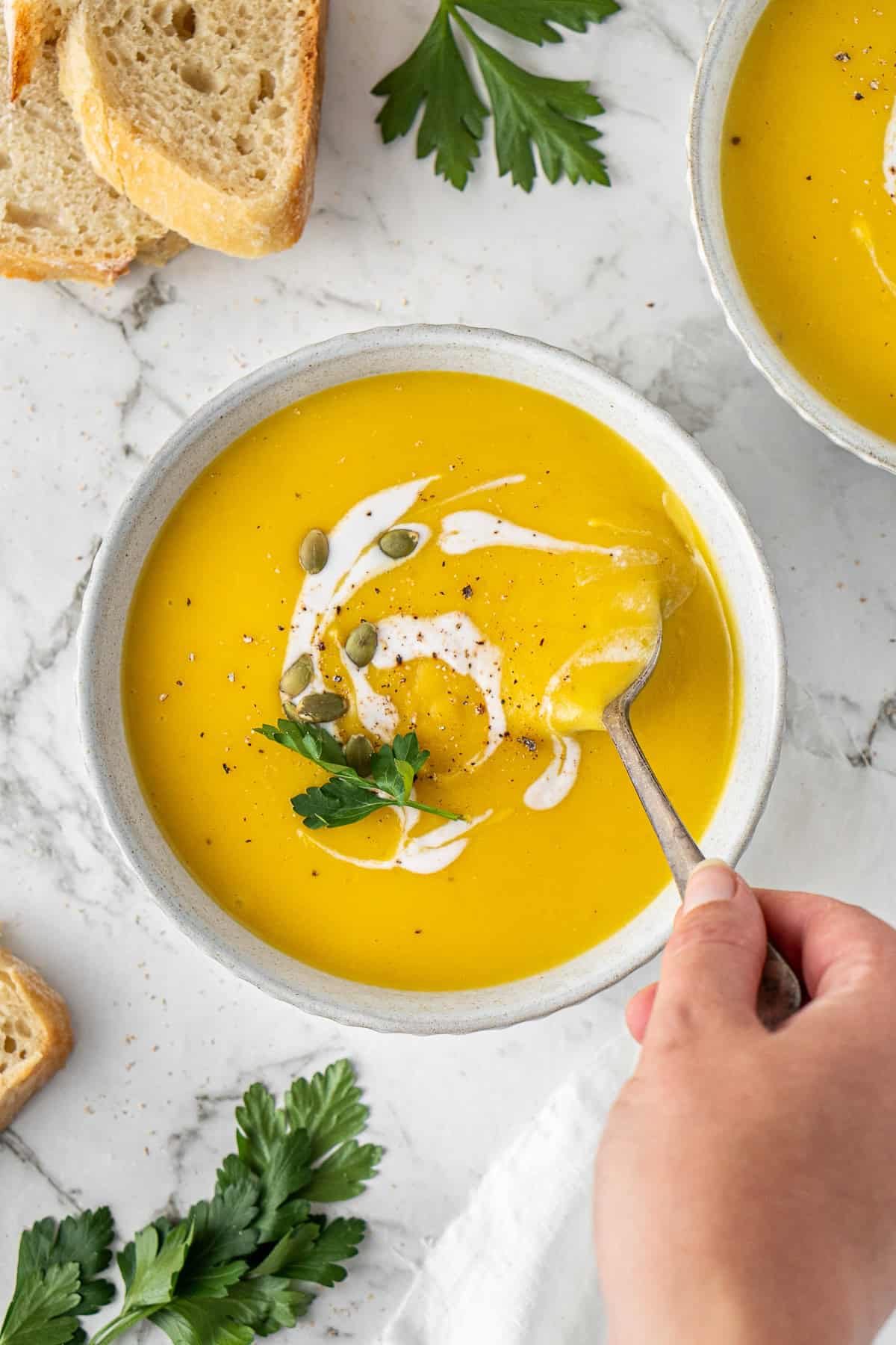 Dairy free pumpkin soup in a bowl with a hand putting in a spoon.