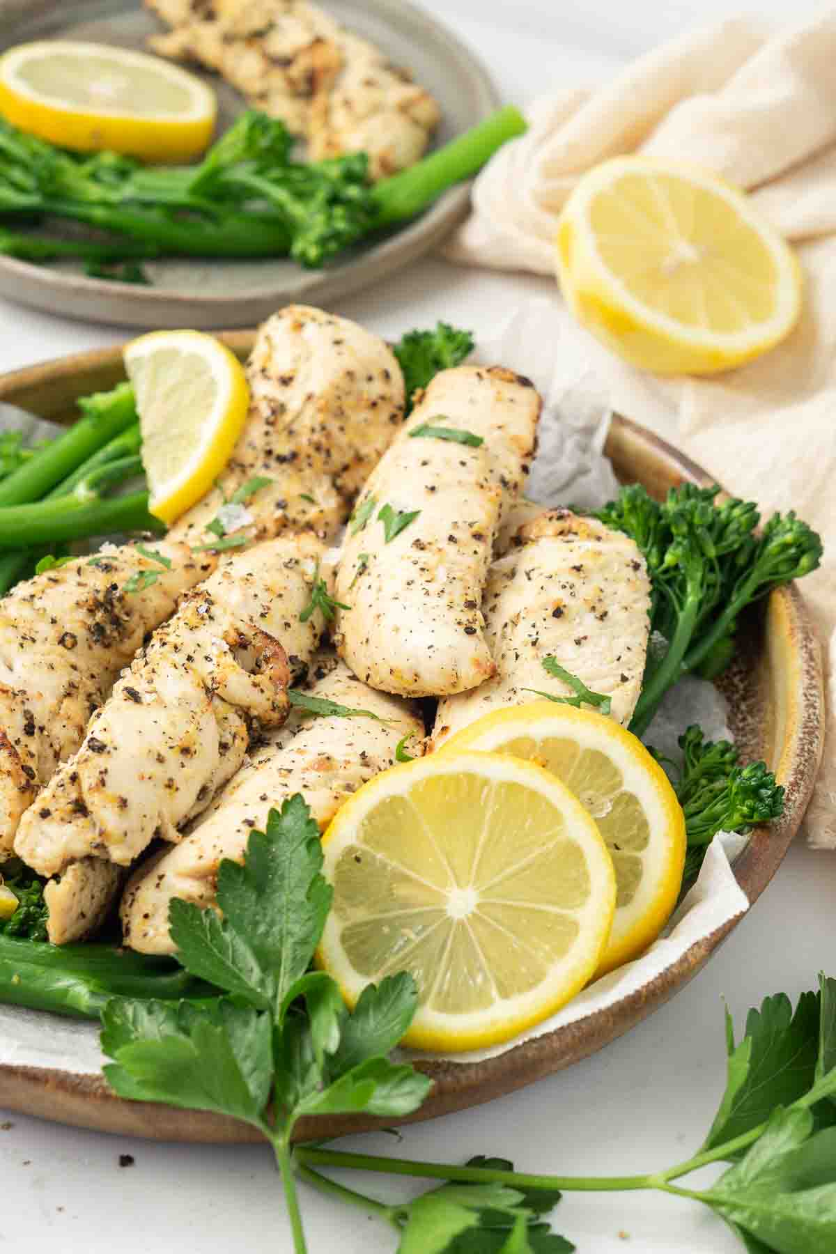 Lemon pepper chicken cooked on a plate with lemon and broccolini. 