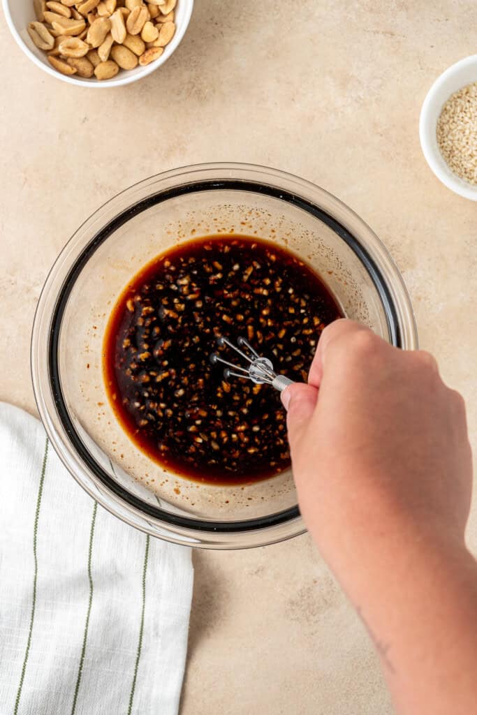 A hand mixing up the sauce ingredients in a small glass bowl.