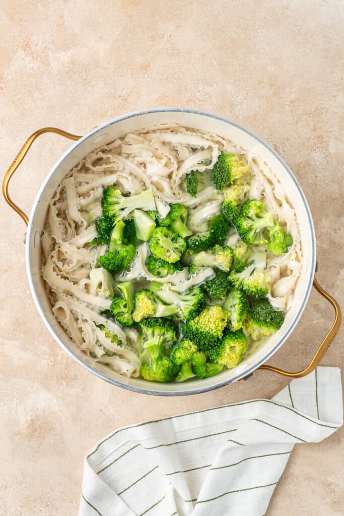 The noodles and broccoli boiling in a large pot.