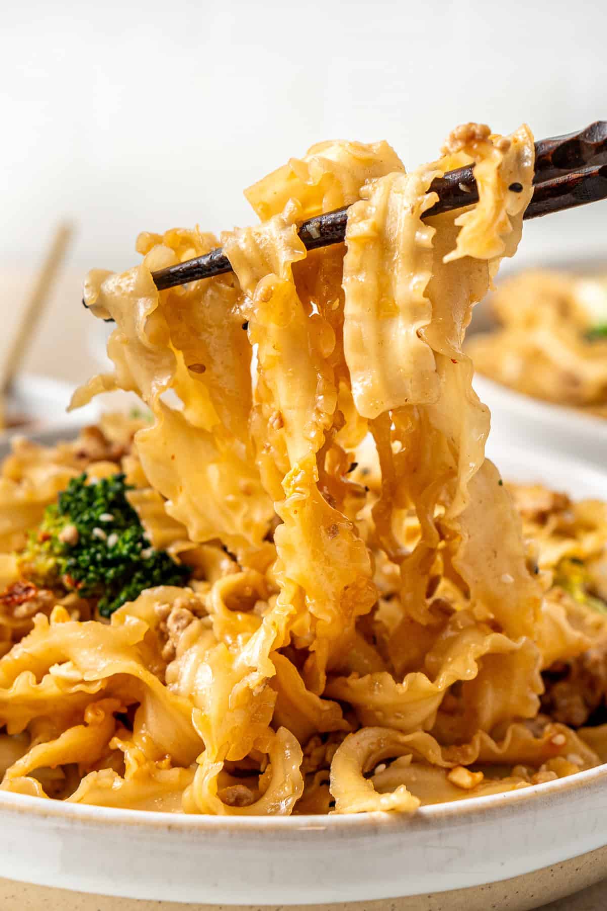 Close up of chopsticks pulling up saucy noodles from a bowl.