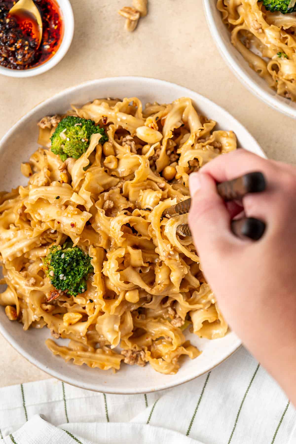 A hand taking a bite of noodles from a white plate.