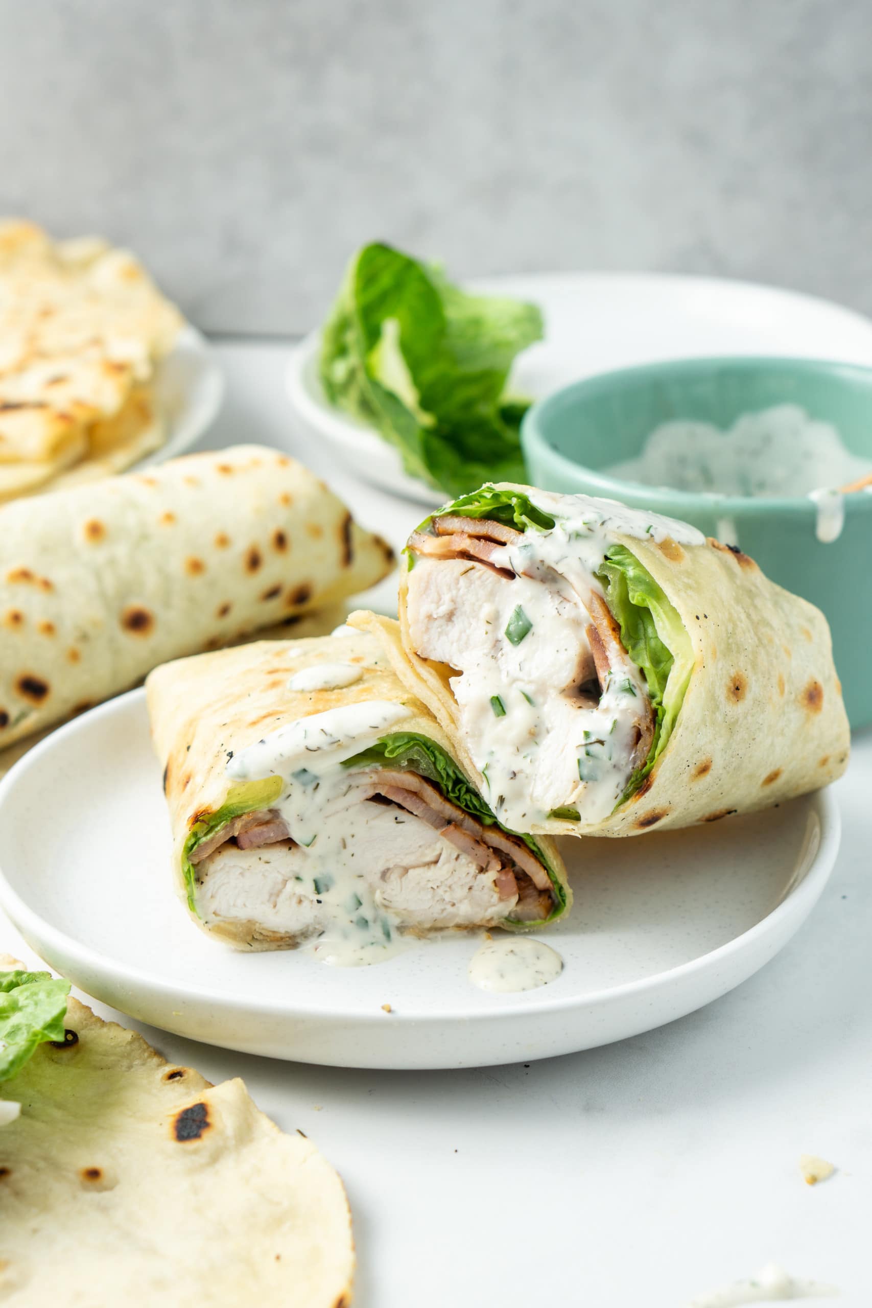Chicken bacon ranch wraps cut in half on a white plate with a drizzle of extra ranch dressing.