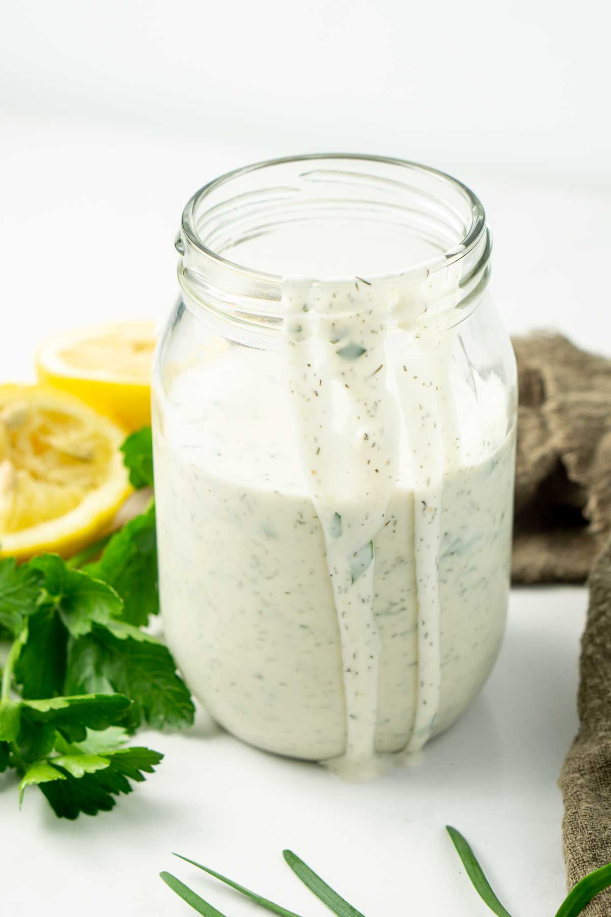 Dairy free ranch dressing in a jar with lemon and parsley in the background and dressing dripping down the sides.