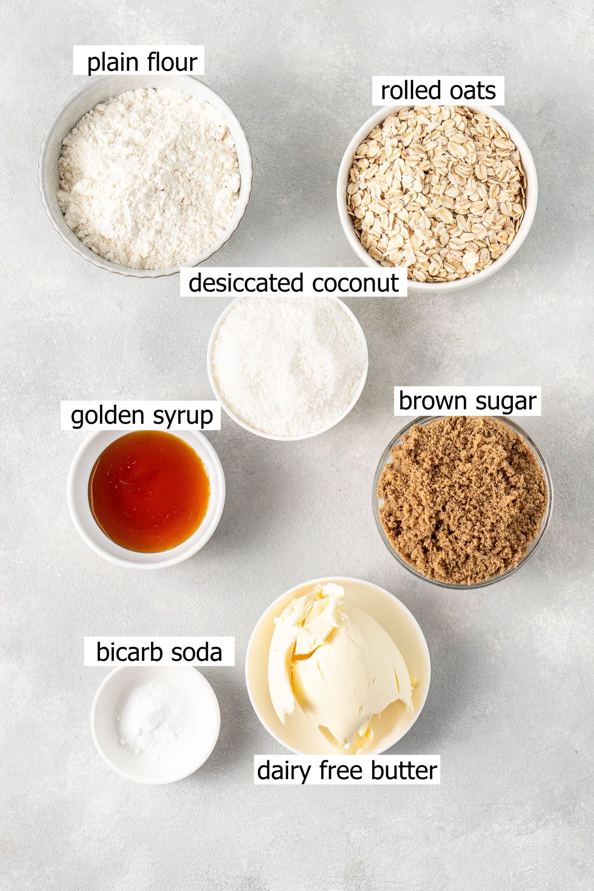 All ingredients needed to make ANZAC biscuits laid out in small bowls.