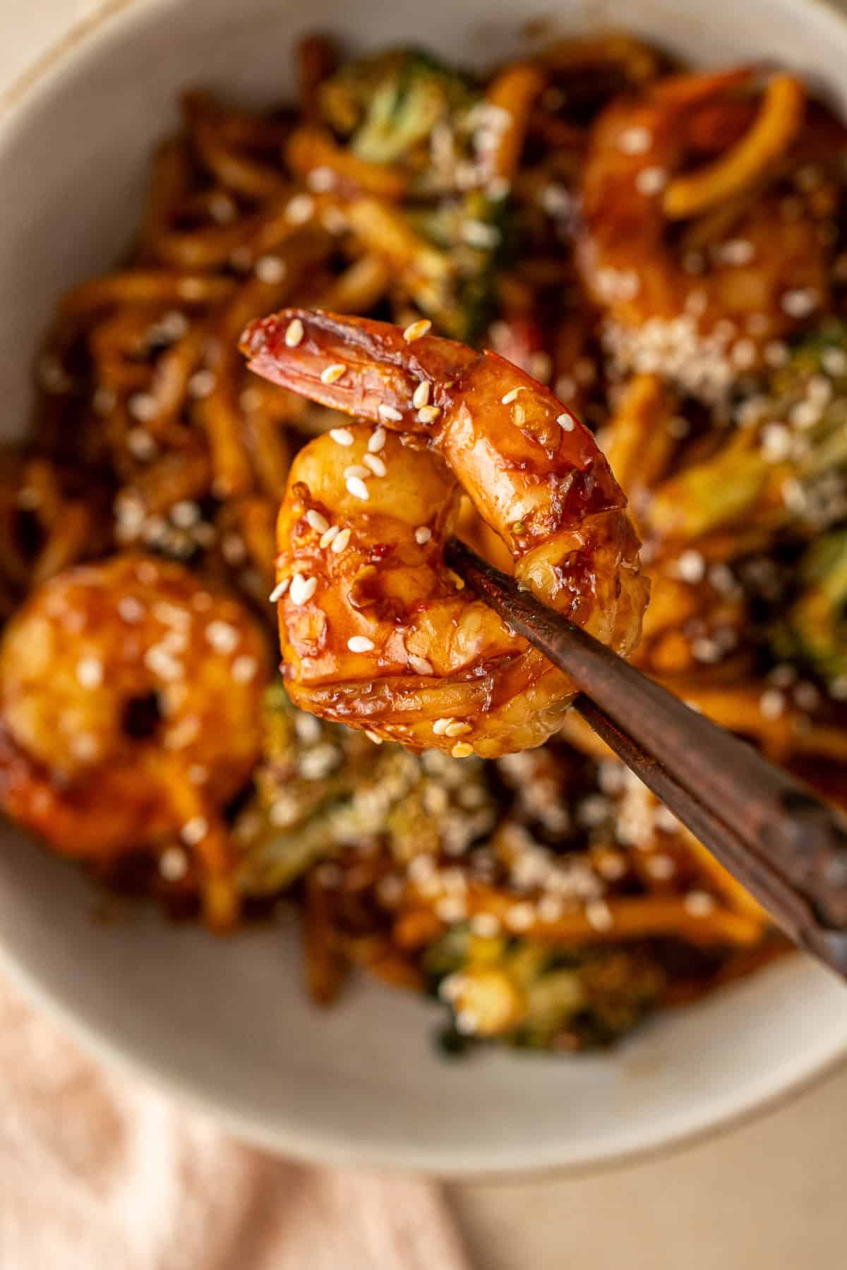 Close up of a prawn being held up with chopsticks. 