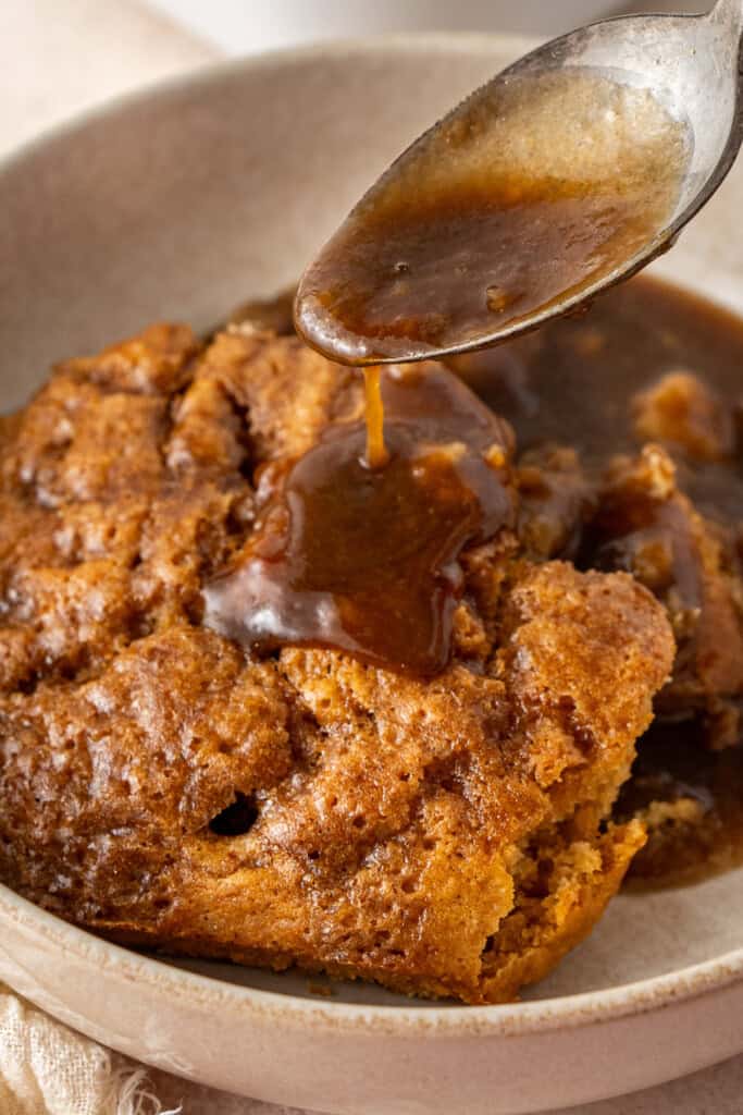 Drizzling the sauce over the pudding in a bowl.