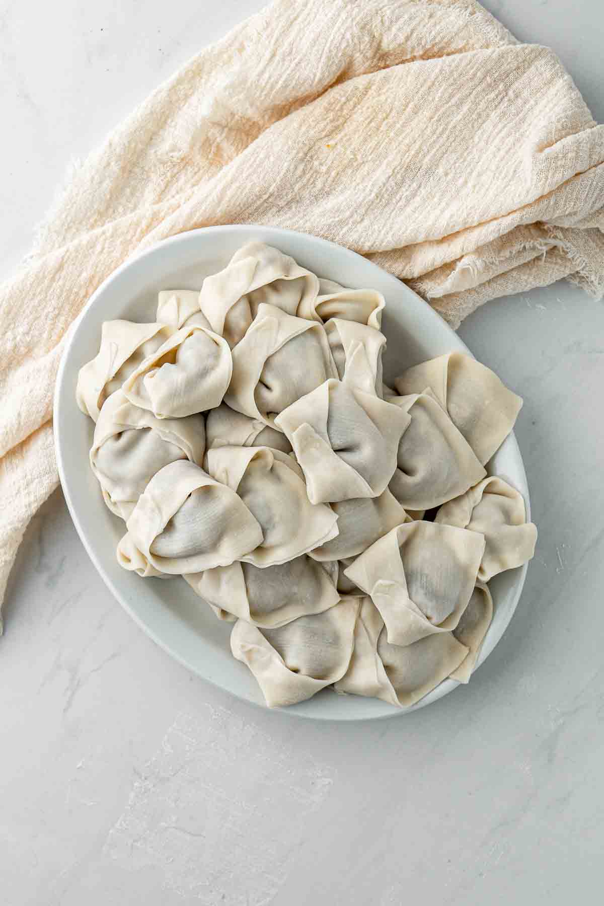 Filled wontons folded and ready to cook on a plate.