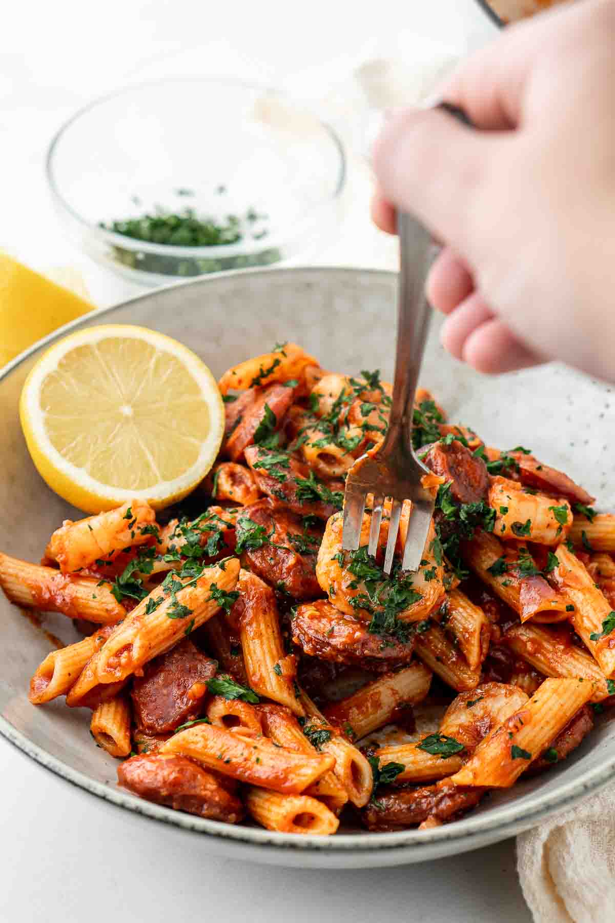 Fork taking a bite of prawn and chorizo pasta with parsley and lemon.