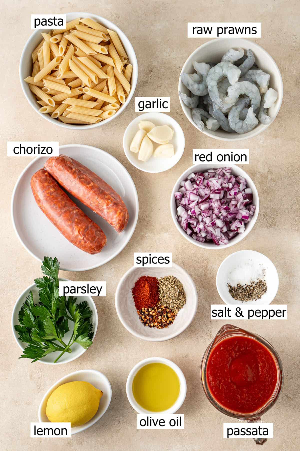 All ingredients needed to make prawn and chorizo pasta laid out in small bowls.