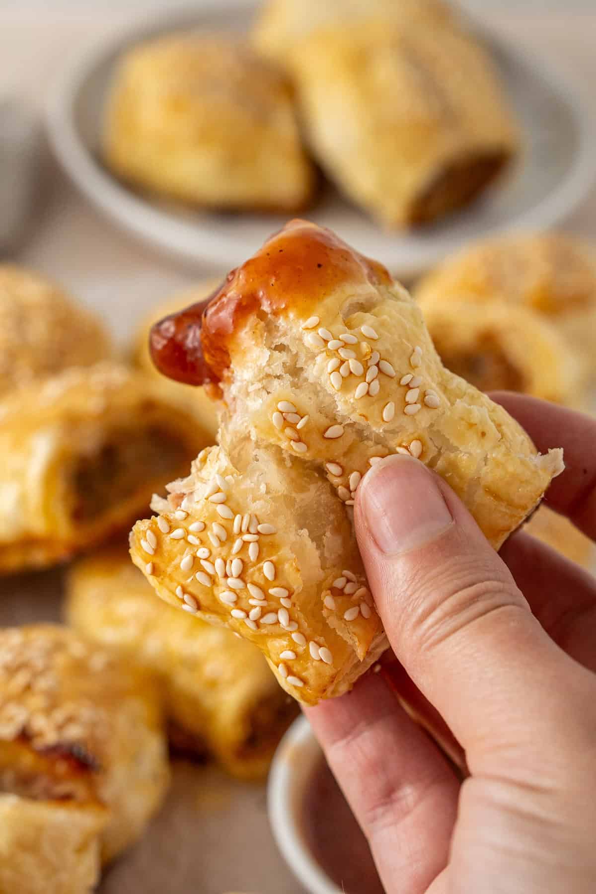 A hand holding a mini sausage roll dunked in tomato sauce with a bite taken.