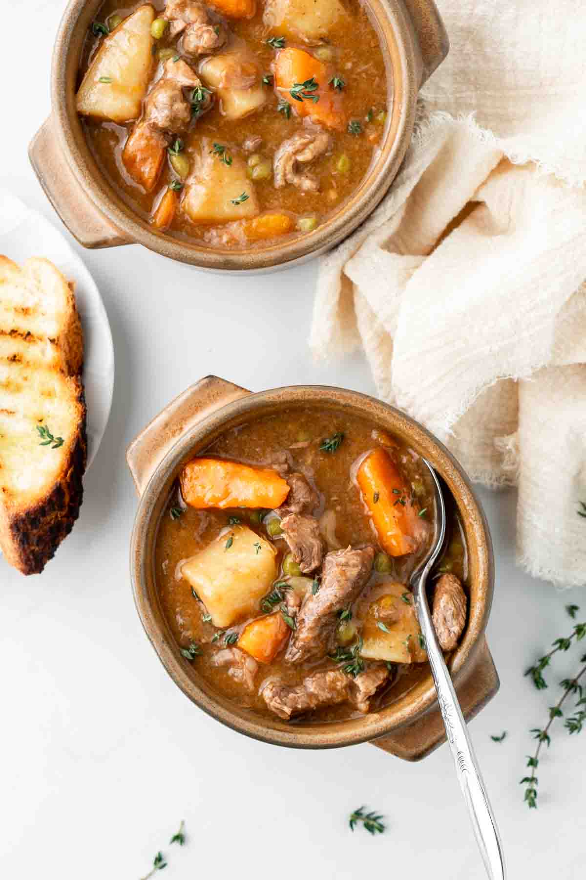 Close up of beef stew with potatoes and carrots with a side of toasted bread.