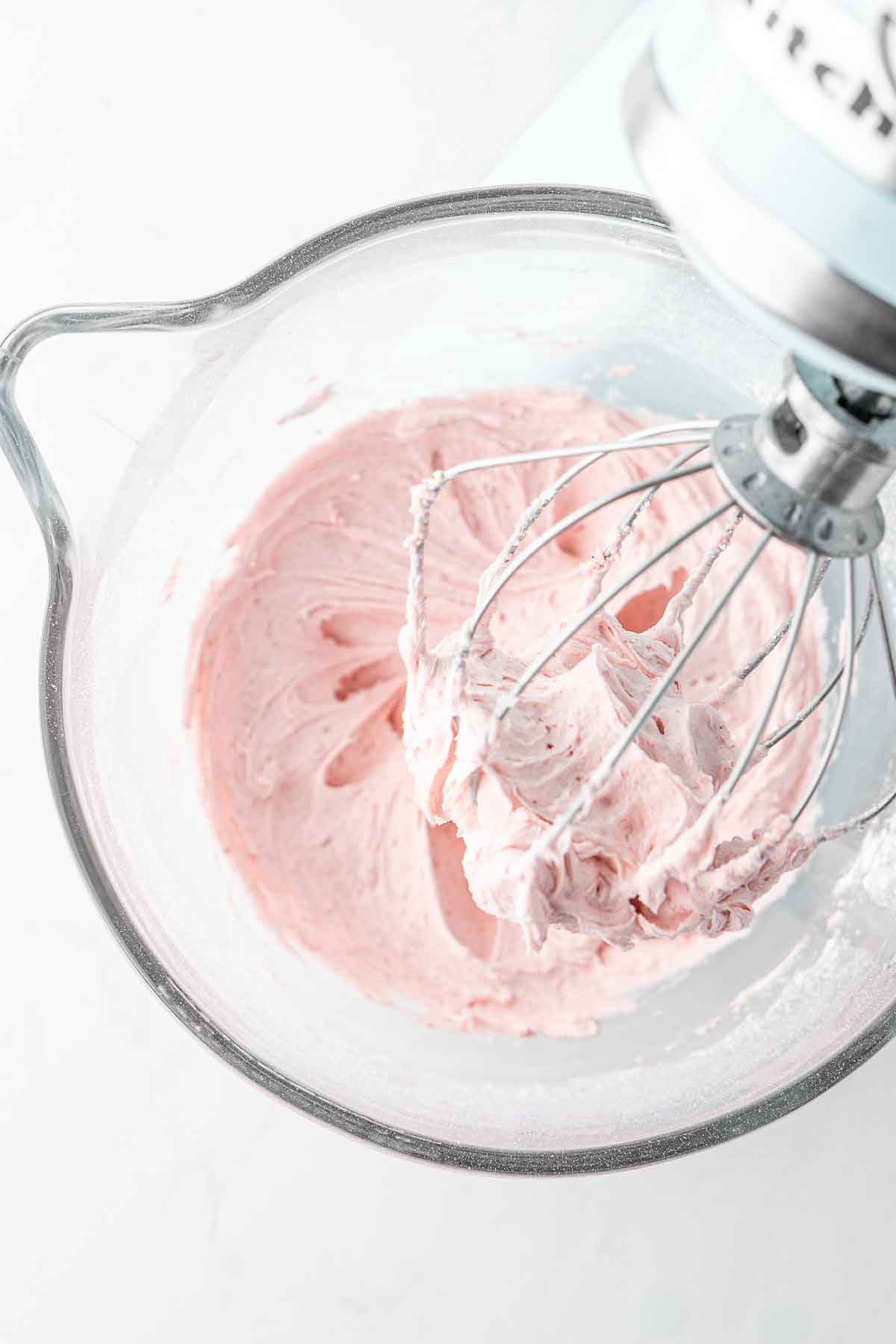 Creamy strawberry buttercream in a stand mixer with a whisk attachement.