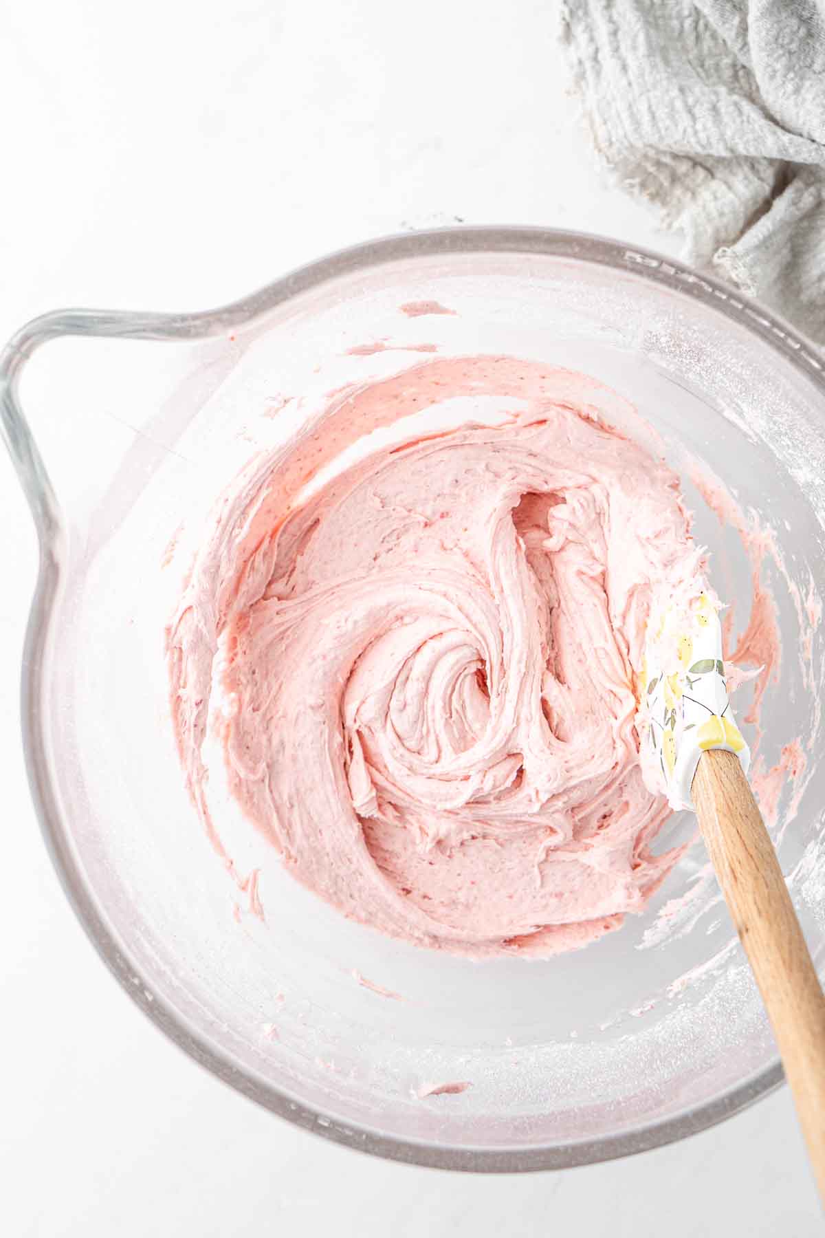 Creamy pink strawberry buttercream in a glass bowl with a spatula. 
