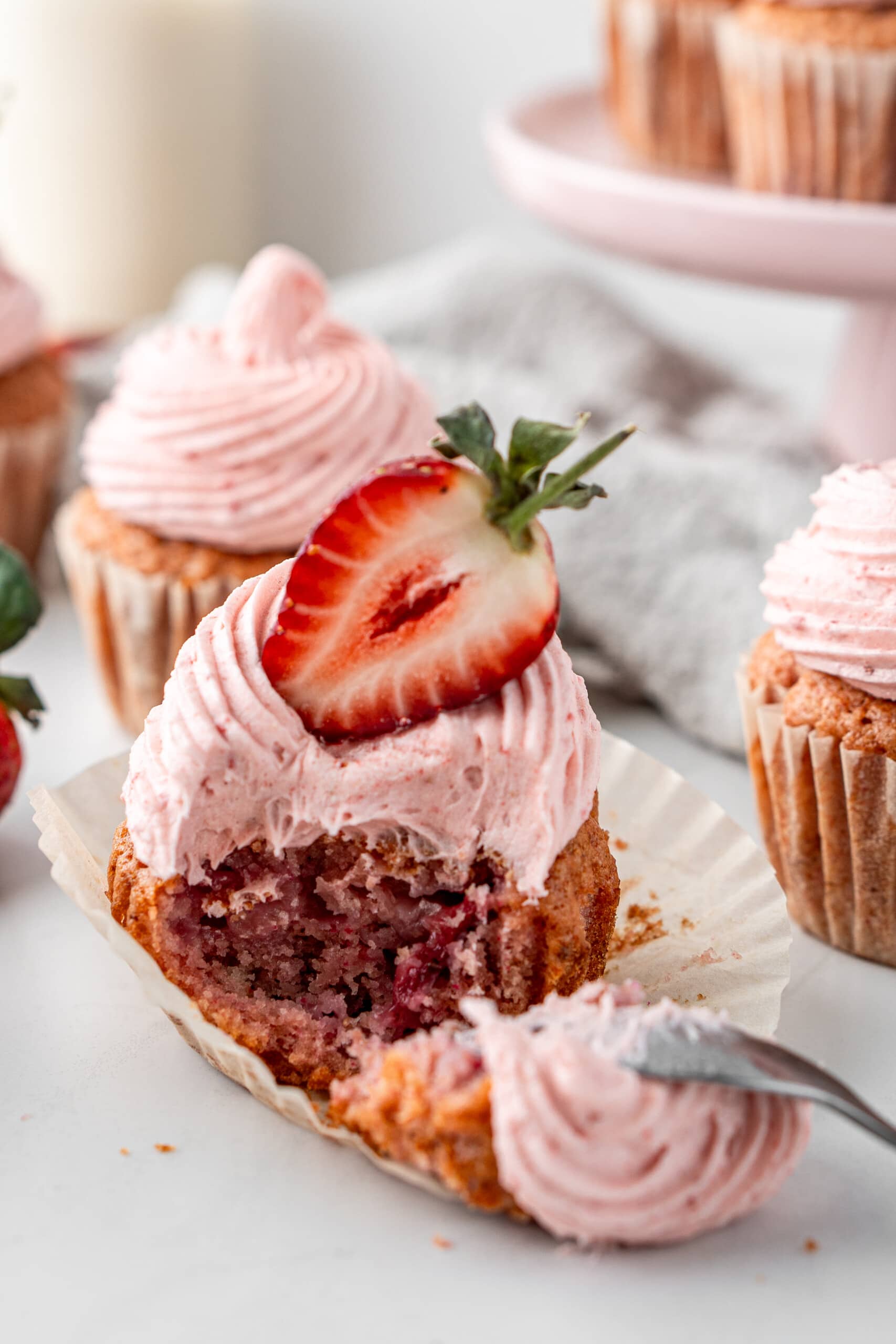 Strawberry cupcakes with a strawberry on top and a spoon taking a bite.