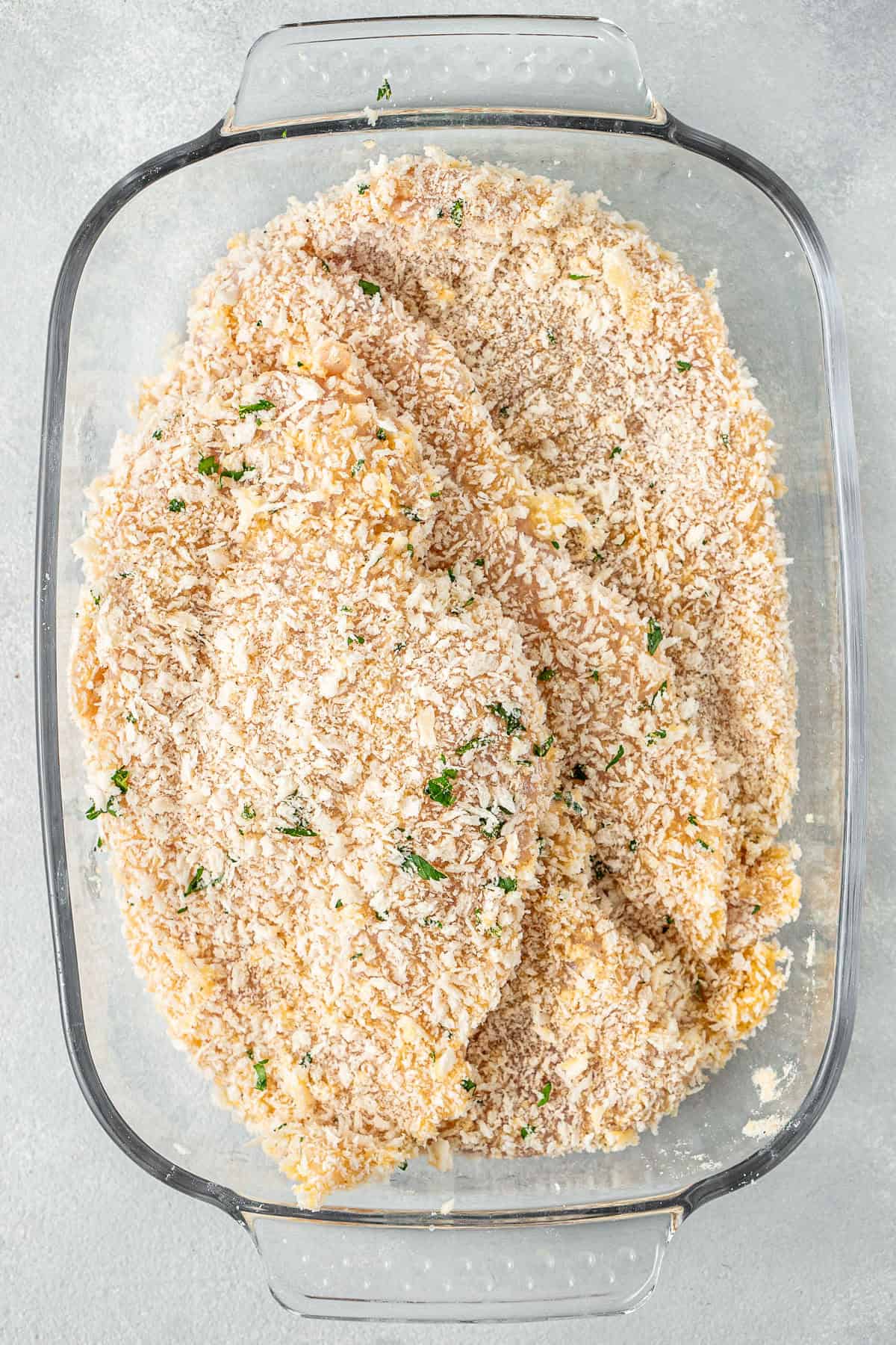 The chicken fillets breaded in a glass dish.