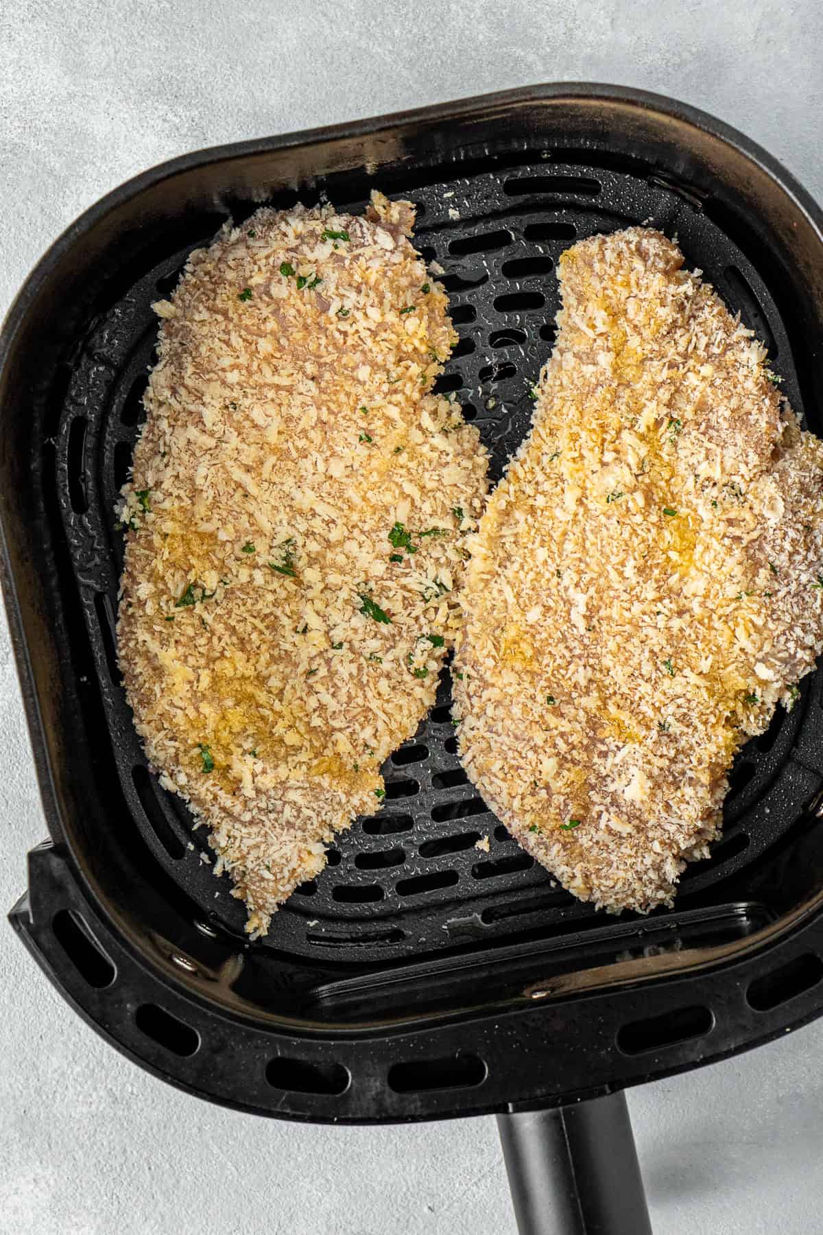 The chicken schnitzels in the basket of the air fryer.