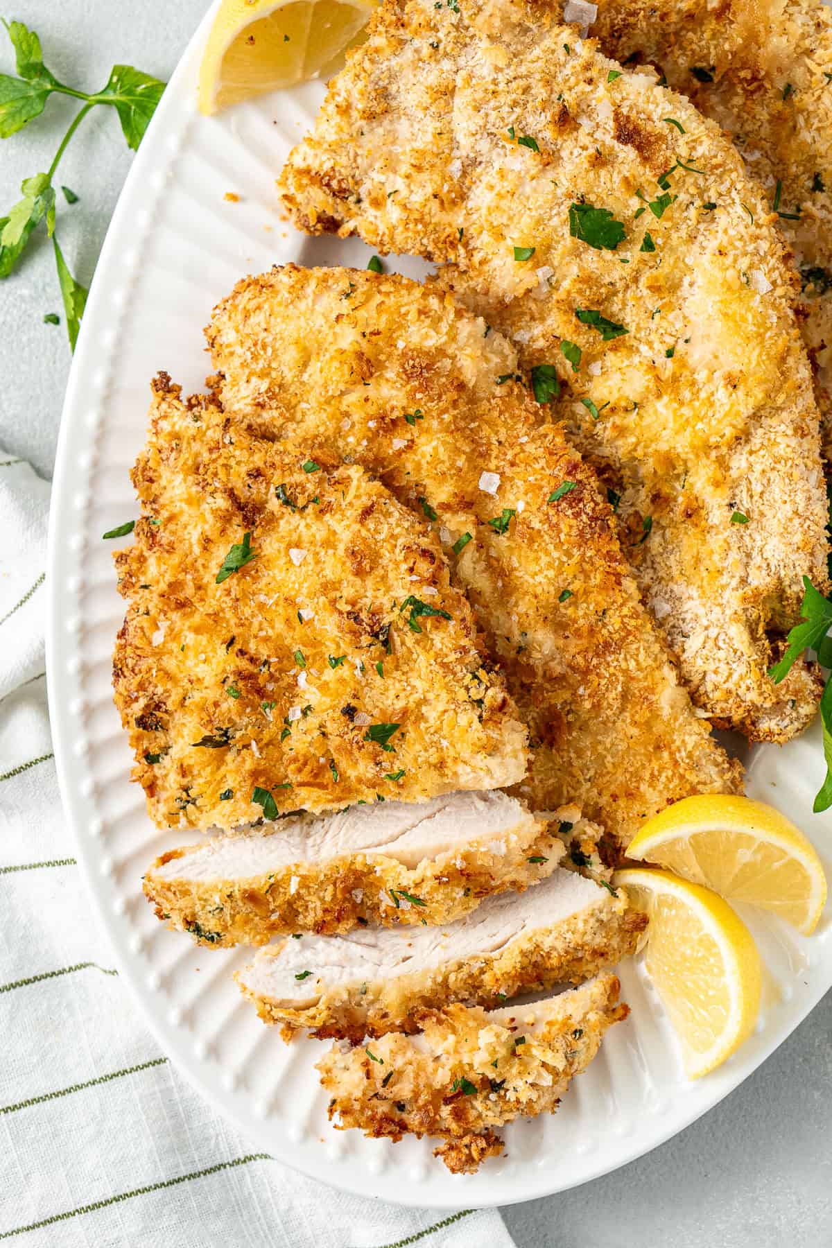 Chicken schnitzels on a white plate with lemon wedges.