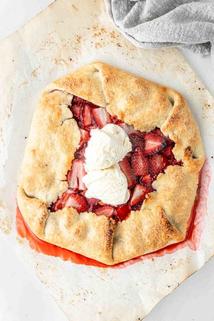 Freshly baked strawberry galette on baking paper with vanilla ice cream.