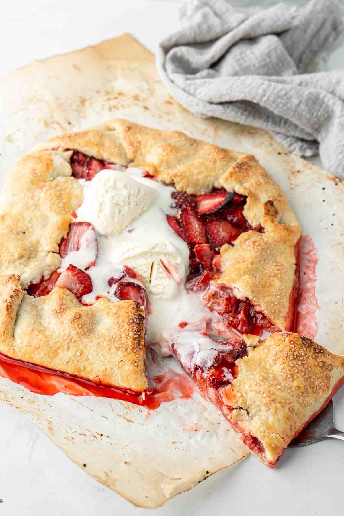 Strawberry galette on baking paper with melted ice cream and a slice being served.