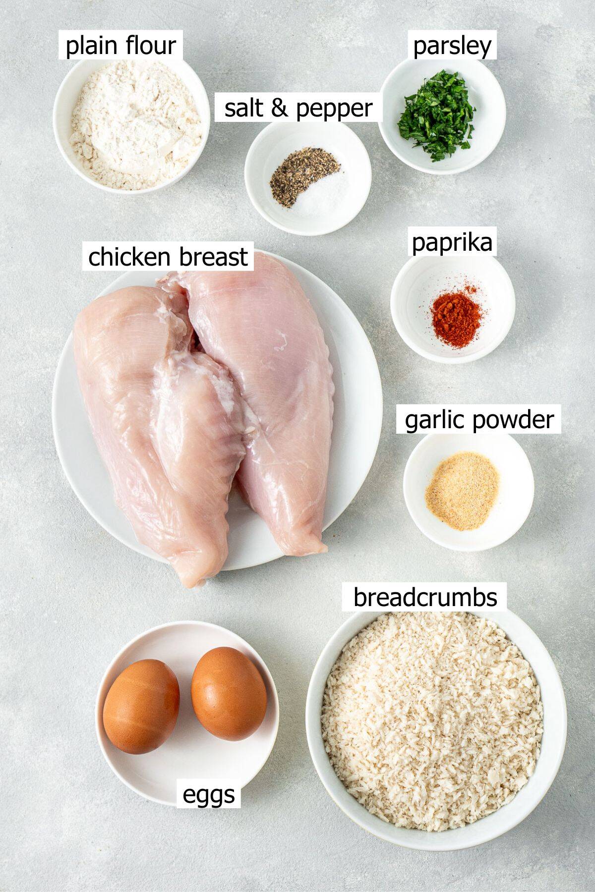 All ingredients needed to make chicken schnitzels laid out in small bowls.