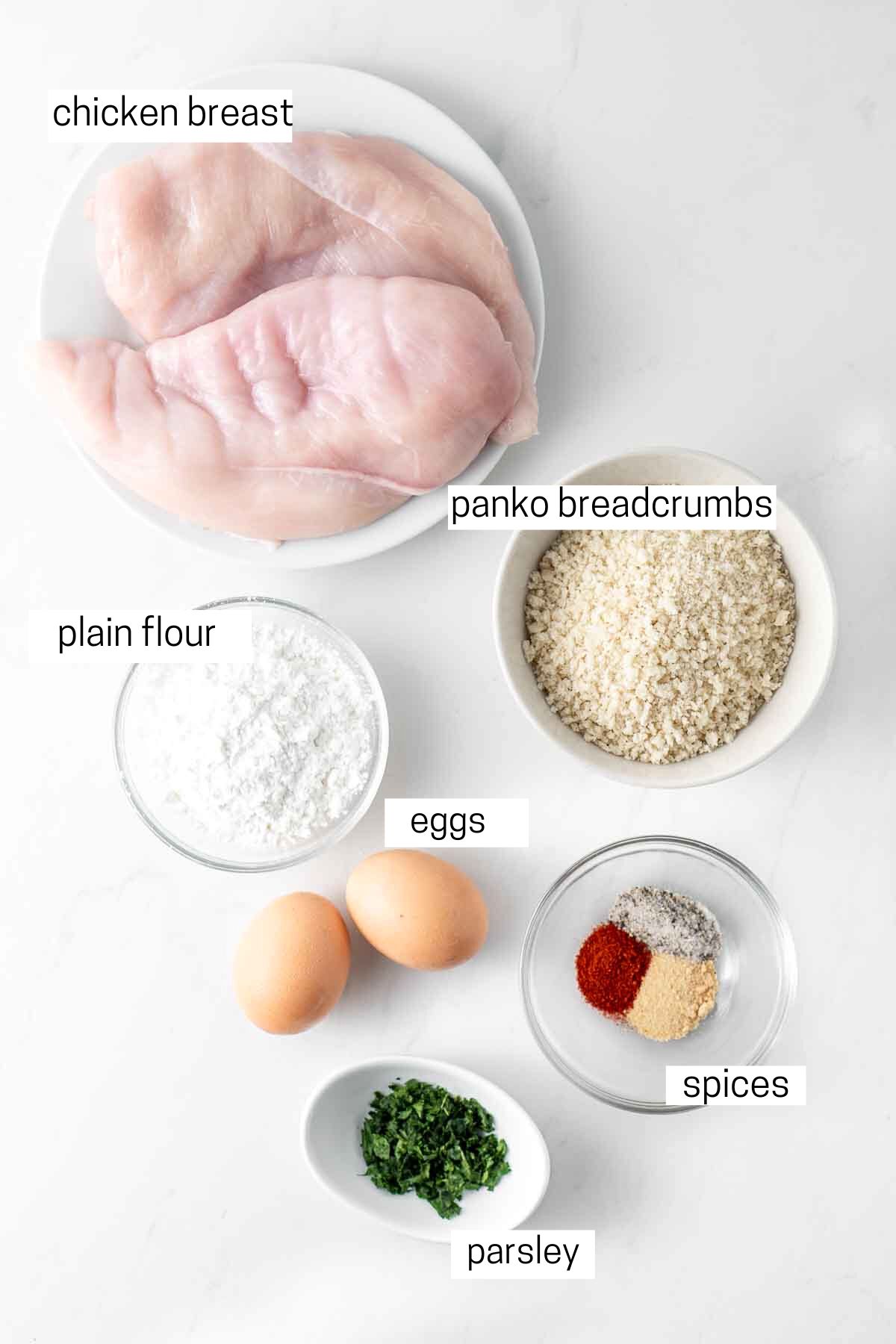 All ingredients needed for chicken schnitzel laid out in small bowls.