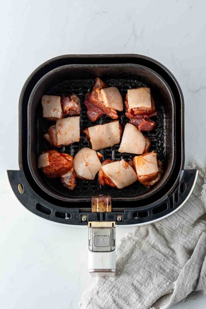 Marinated pork belly bites in the basket of the air fryer ready for cooking.