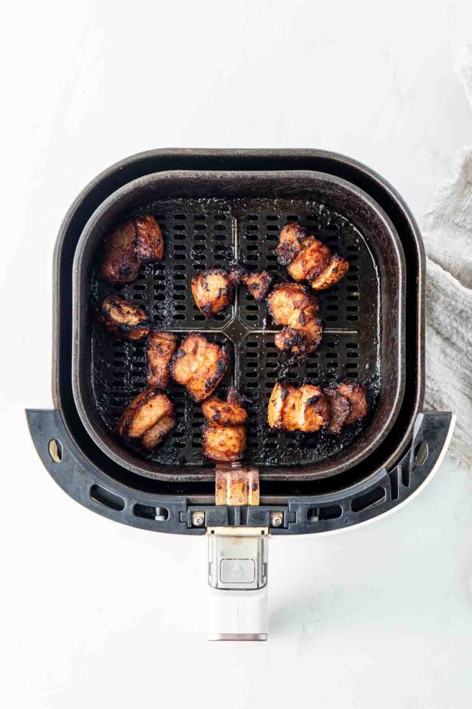 Cooked pork belly bites in the basket of the air fryer.