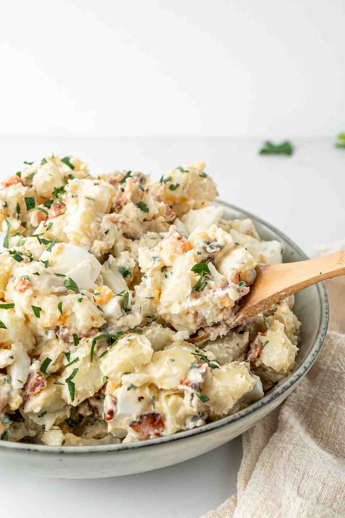 Wooden spoon serving potato salad from a bowl.